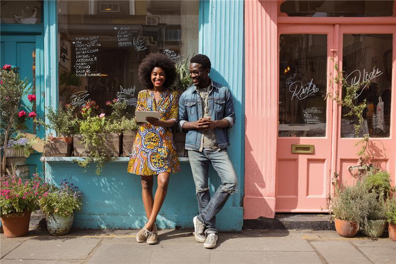 Two young entrepreneurs stand at their storefront, chatting about their growing businesses.